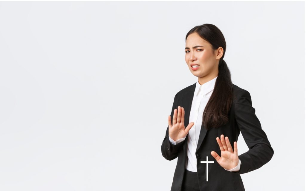 TheREDWords.website/BLOG page. A photo of a young woman dressed in a black suit. She is holding her hands out in refusal of the cross.