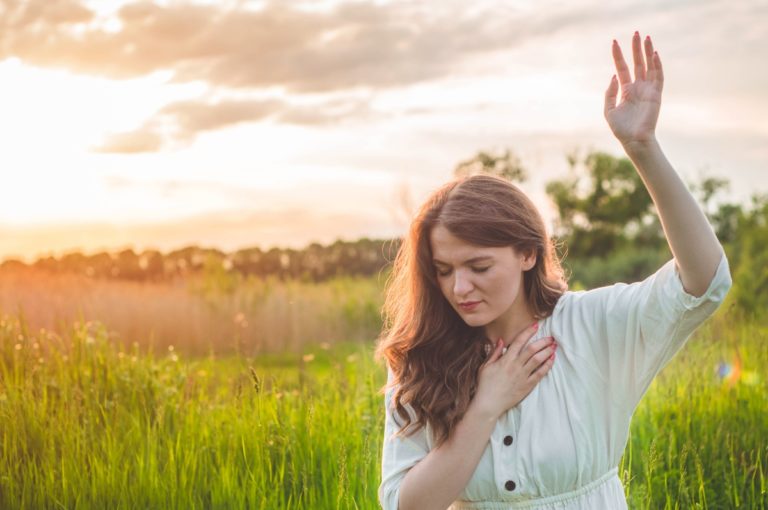 TheREDWords.website/BLOG page. A photo of a woman standing in a field at sunset with one hand raised toward heaven.