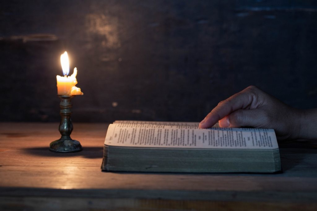 TheREDWords.website/BLOG page. A photo of the open Holy Bible in candlelight. A hand traces scripture.