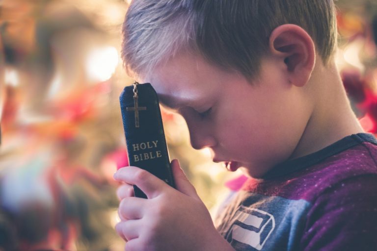 TheREDWords.website/BLOG page. A photo of a child holding the Holy Bible up to his forehead as he prays.