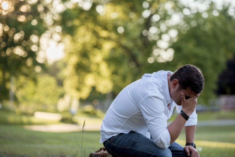 TheREDWords.website/BLOG page. Photo of a man in a beautiful park. He's on his knees and one hand covers his face.